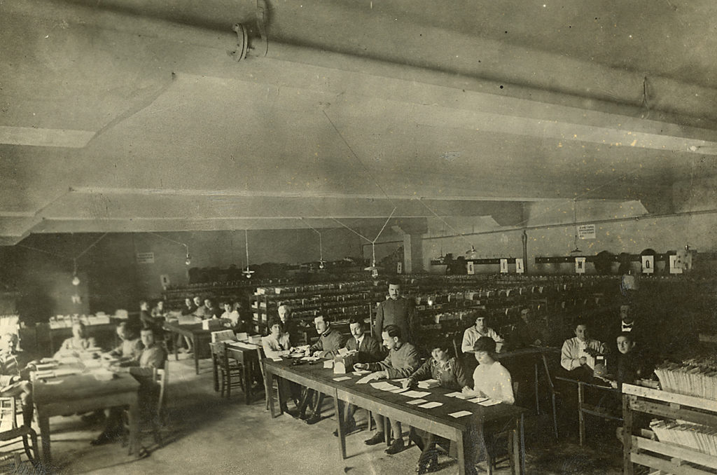 Scrivere la Grande Guerra. Donne e uomini al lavoro in un ufficio postale durante la Grande Guerra. Foto Archivio Touring Club Italiano [CC BY-SA 3.0]
