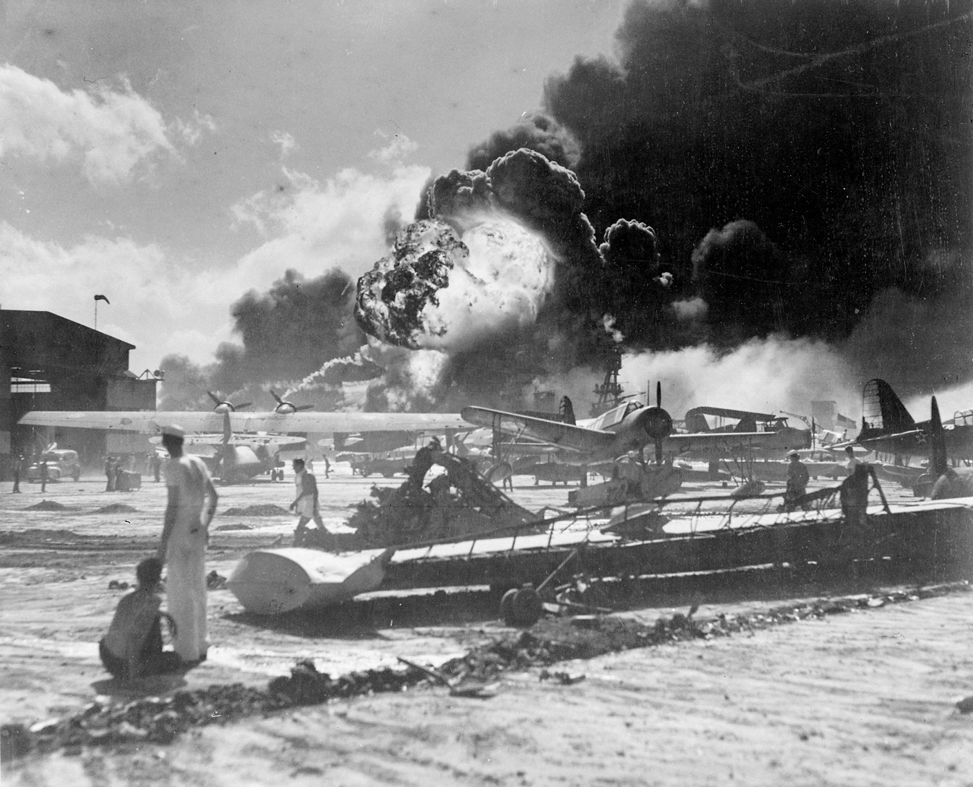 Aerei statunitensi danneggiati durante l'attacco di Pearl Harbor a Ford Island. Sullo sfondo si vede la nave USS Shaw in fiamme. USN - Official U.S. Navy photograph 80-G-19948